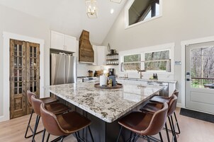 A modern kitchen with a large island, bar stools, and a view of the outdoors through a window.