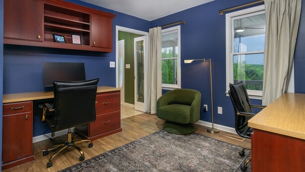 Une pièce comprenant un bureau, deux chaises, un ventilateur de plafond et une fenêtre avec des rideaux.