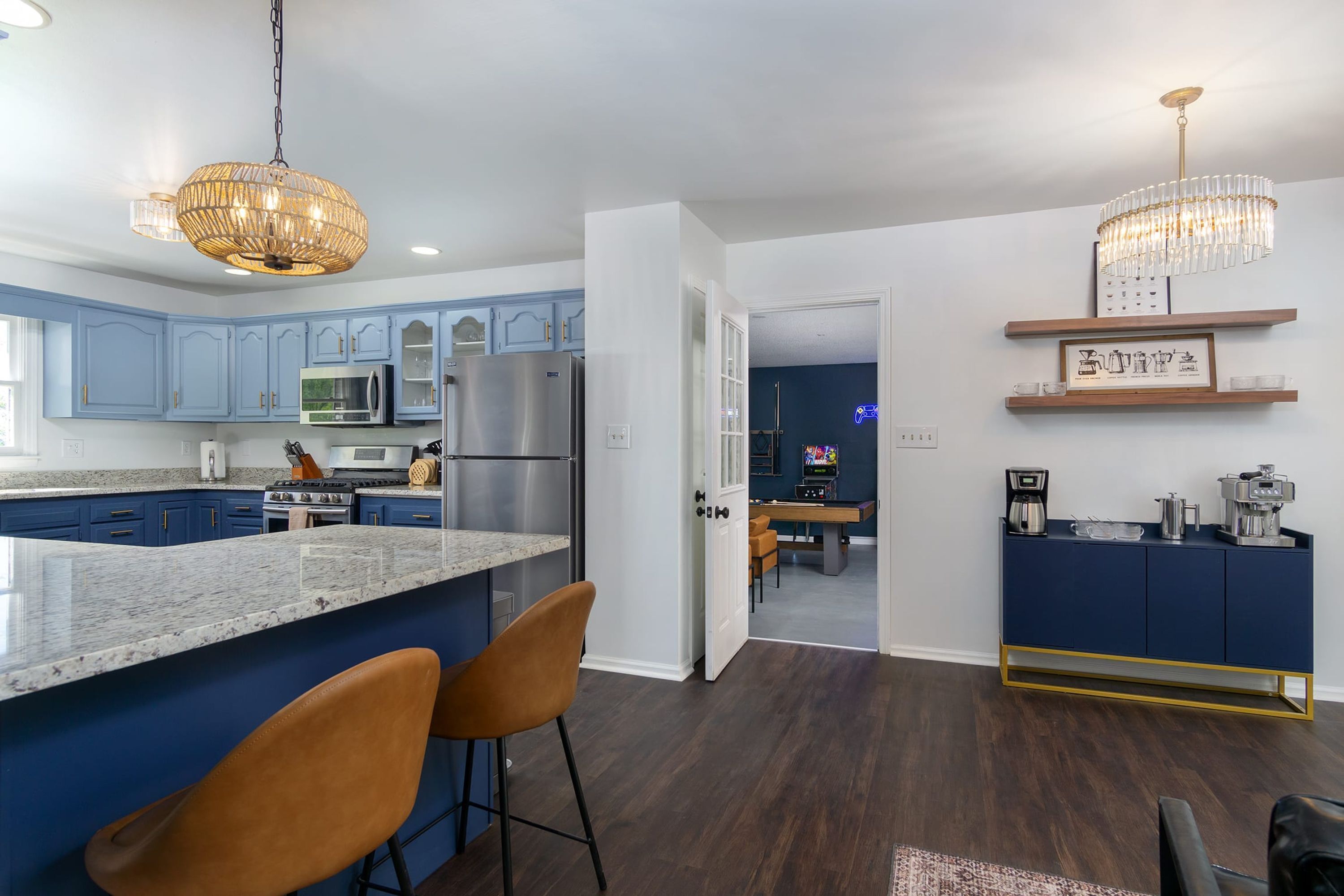 A modern kitchen with blue cabinets, stainless steel appliances, and a marble island with two bar stools.