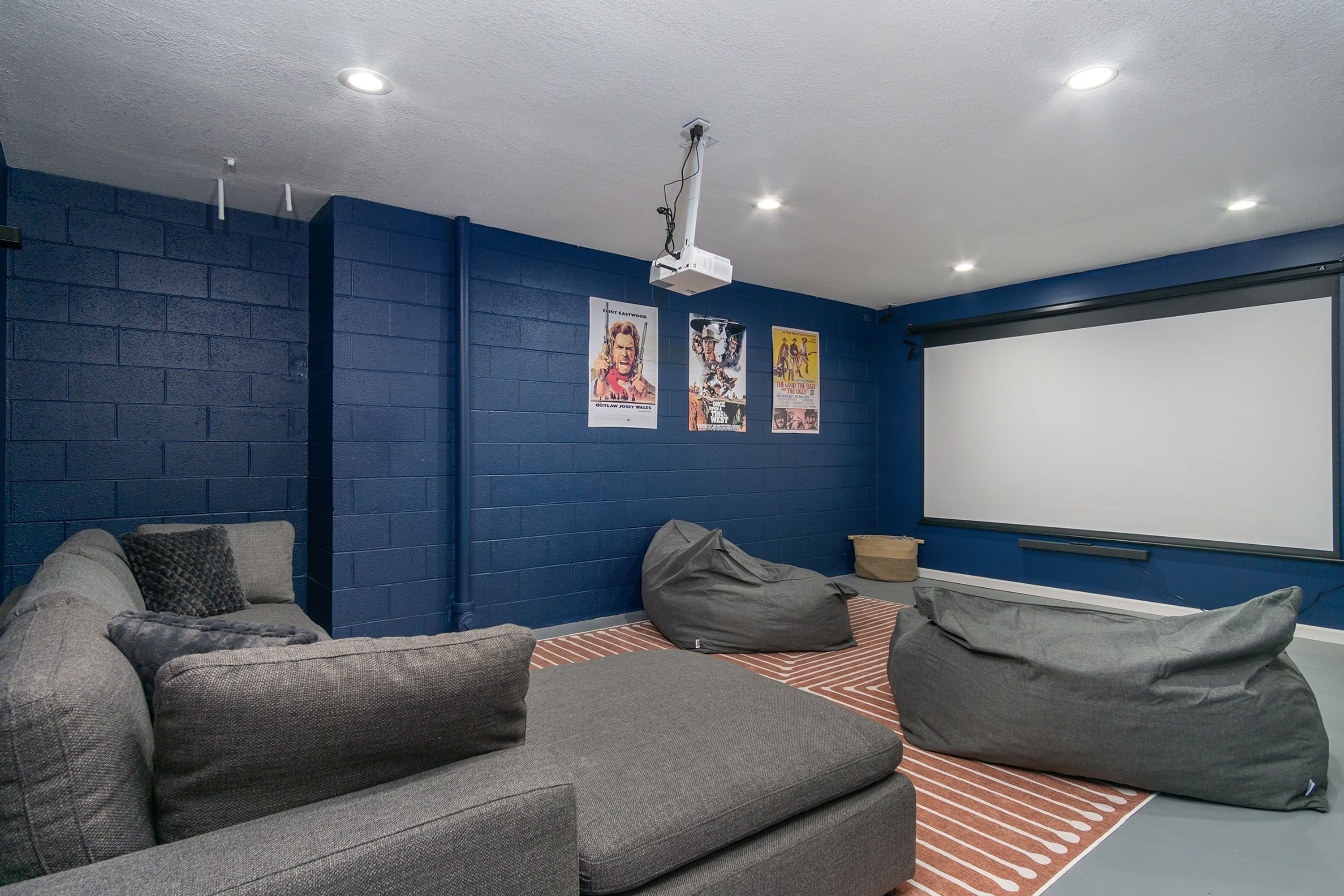 A room with a blue brick wall, a white ceiling, a projector, a white screen, a grey sofa, and a bean bag.