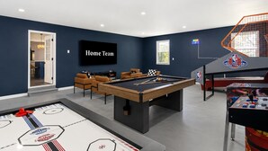 Une salle de divertissement équipée d’une table de billard, de sièges, d’un téléviseur et d’une borne d’arcade de basketball.