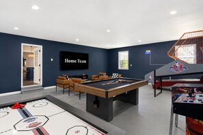 A home entertainment room with a pool table, seating, a television, and a basketball arcade. - Massive Asheville Compound A Memorable Experience (Weaverville)