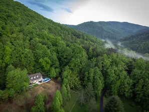 Vue aérienne d’une maison entourée d’une forêt dense, avec une piscine.