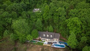 Une maison à deux étages avec une piscine, entourée d’une forêt dense.