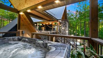 A hot tub on a wooden deck with a stone wall and a view of trees.