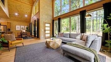 A spacious living room with a large window, a sofa, a coffee table, and a dining area with chairs.