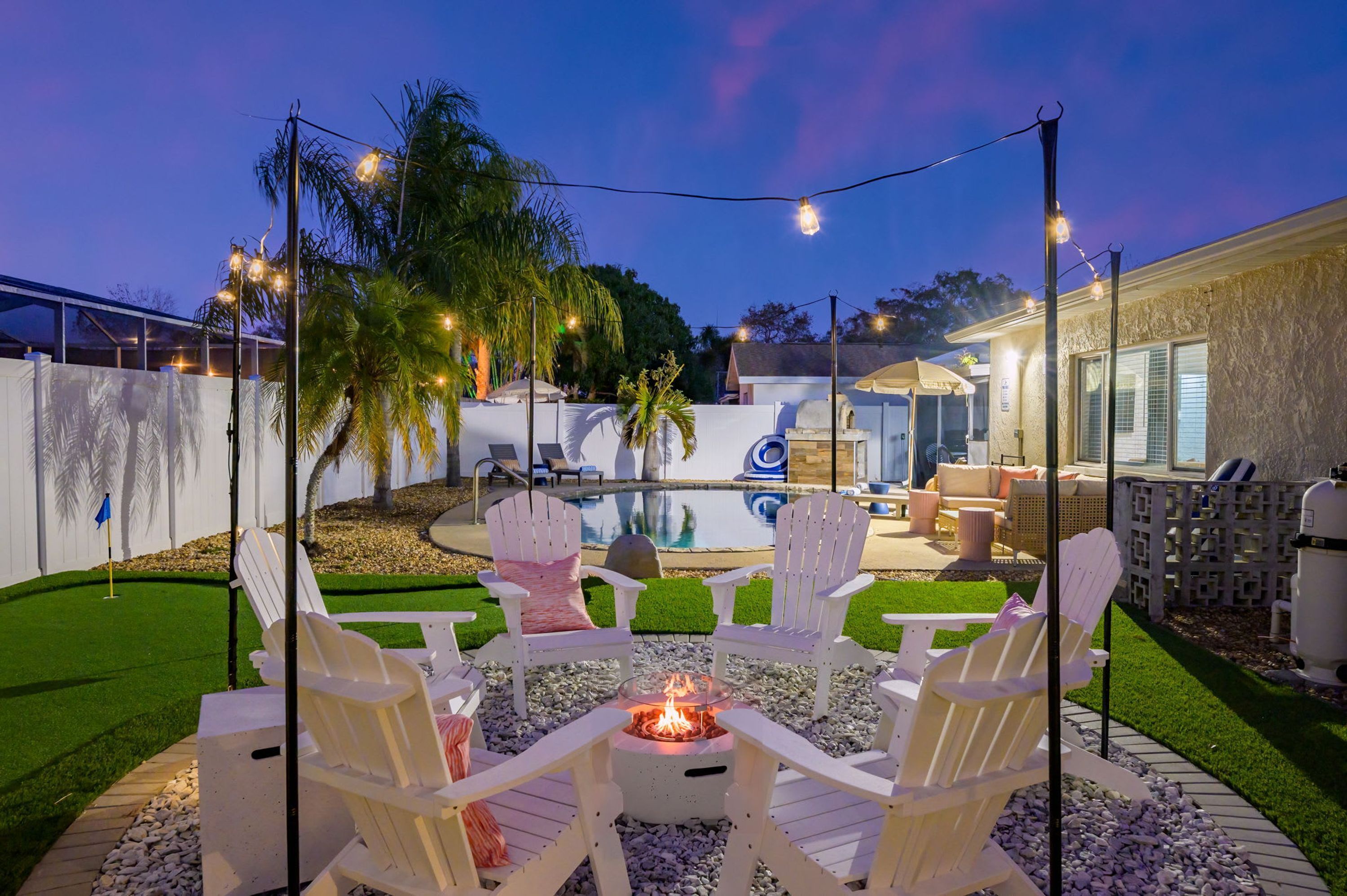 A backyard with a fire pit, outdoor seating, a pool, and string lights.
