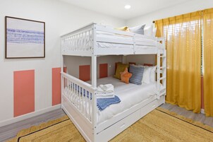 Habitación con literas de estructura blanca, un cuadro en la pared y una cortina amarilla.