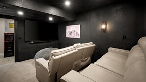 Ein Heimkino mit großem Flachbildfernseher, Liegesesseln und Teppichboden.