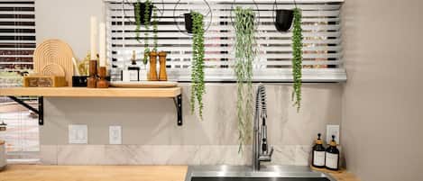 Una cocina moderna con un lavamanos de acero inoxidable, encimera de madera, plantas colgantes y una estantería empotrada con utensilios de cocina.