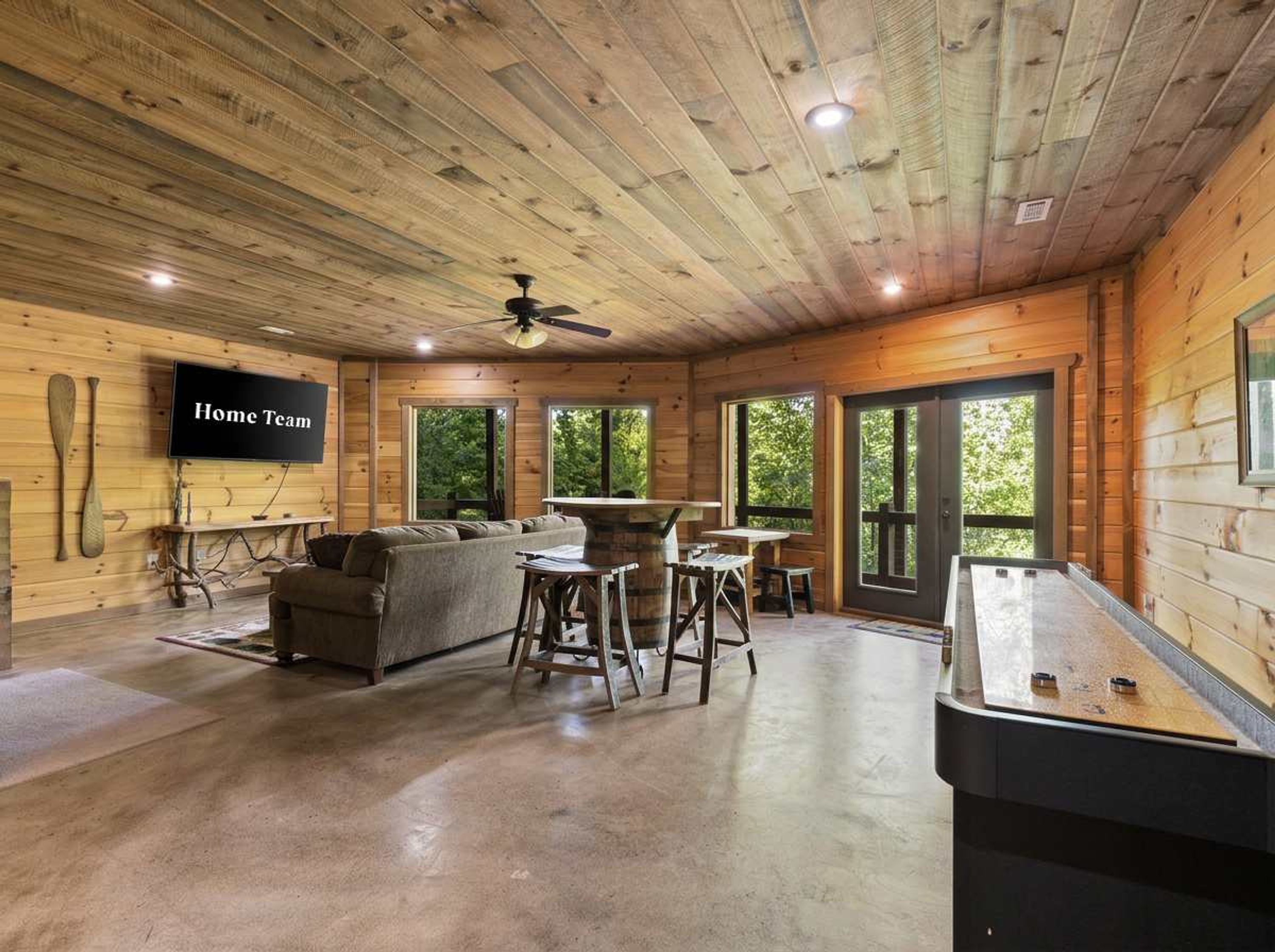 L’intérieur d’un chalet en bois, avec un canapé, une table à manger et un téléviseur au mur sur lequel on peut lire l’inscription « Home Team ».