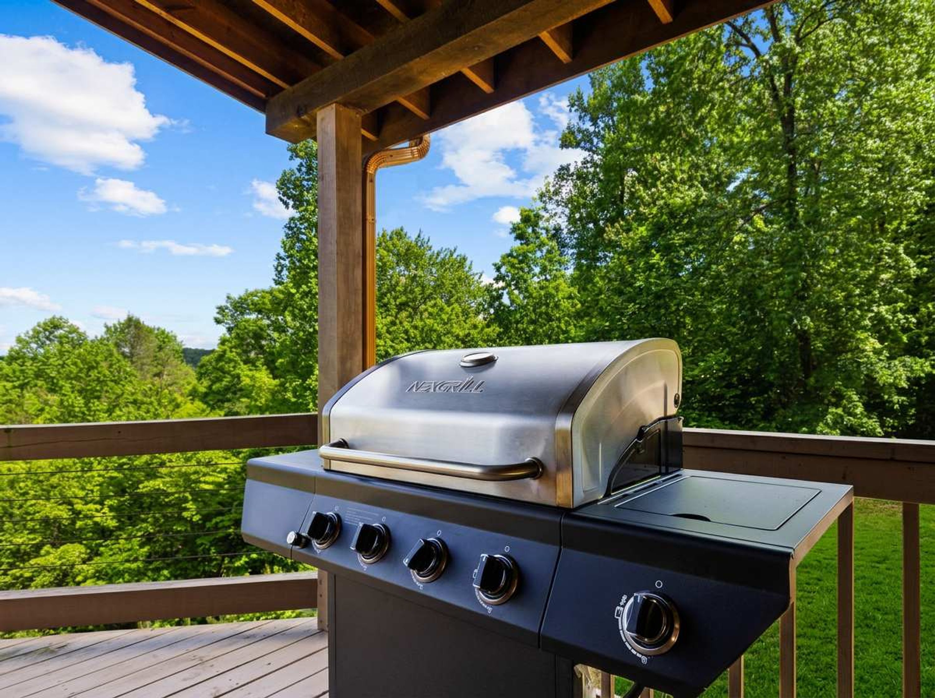 Un barbecue à quatre brûleurs, doté d’un couvercle, installé sur une terrasse extérieure avec une rambarde en bois.