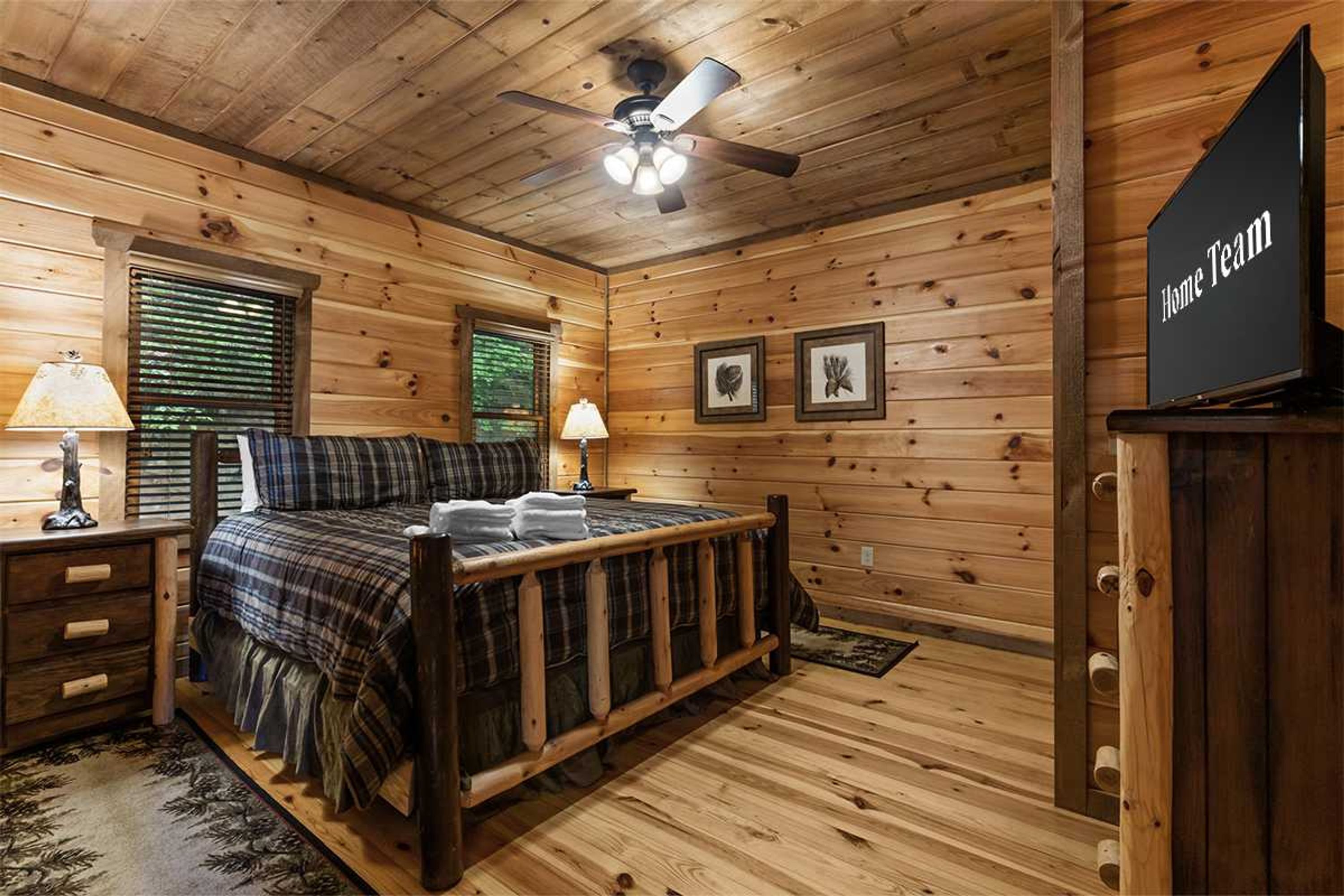 Une chambre dans une cabane en bois, avec un lit, deux lampes de chevet, un ventilateur de plafond et une pancarte sur laquelle on peut lire : « Équipe locale ».