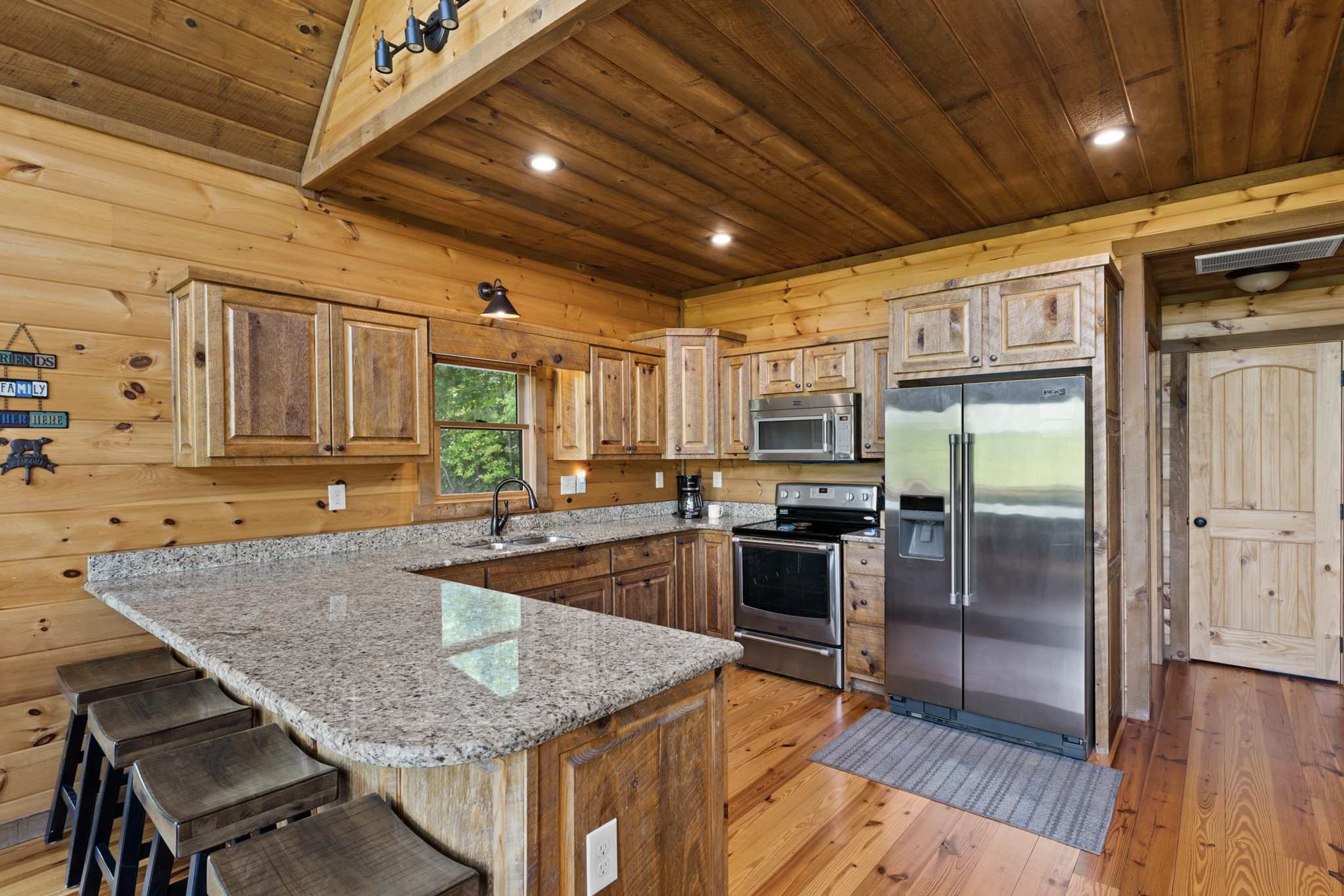 A kitchen with wooden cabinets, granite countertops, stainless steel appliances, and a bar stool area.