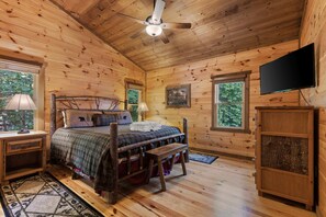 A wooden cabin bedroom with a bed, bedside tables, a television, and windows. - Mtn Cabin w Hot Tub Game Room Grill Views (Blue Ridge)