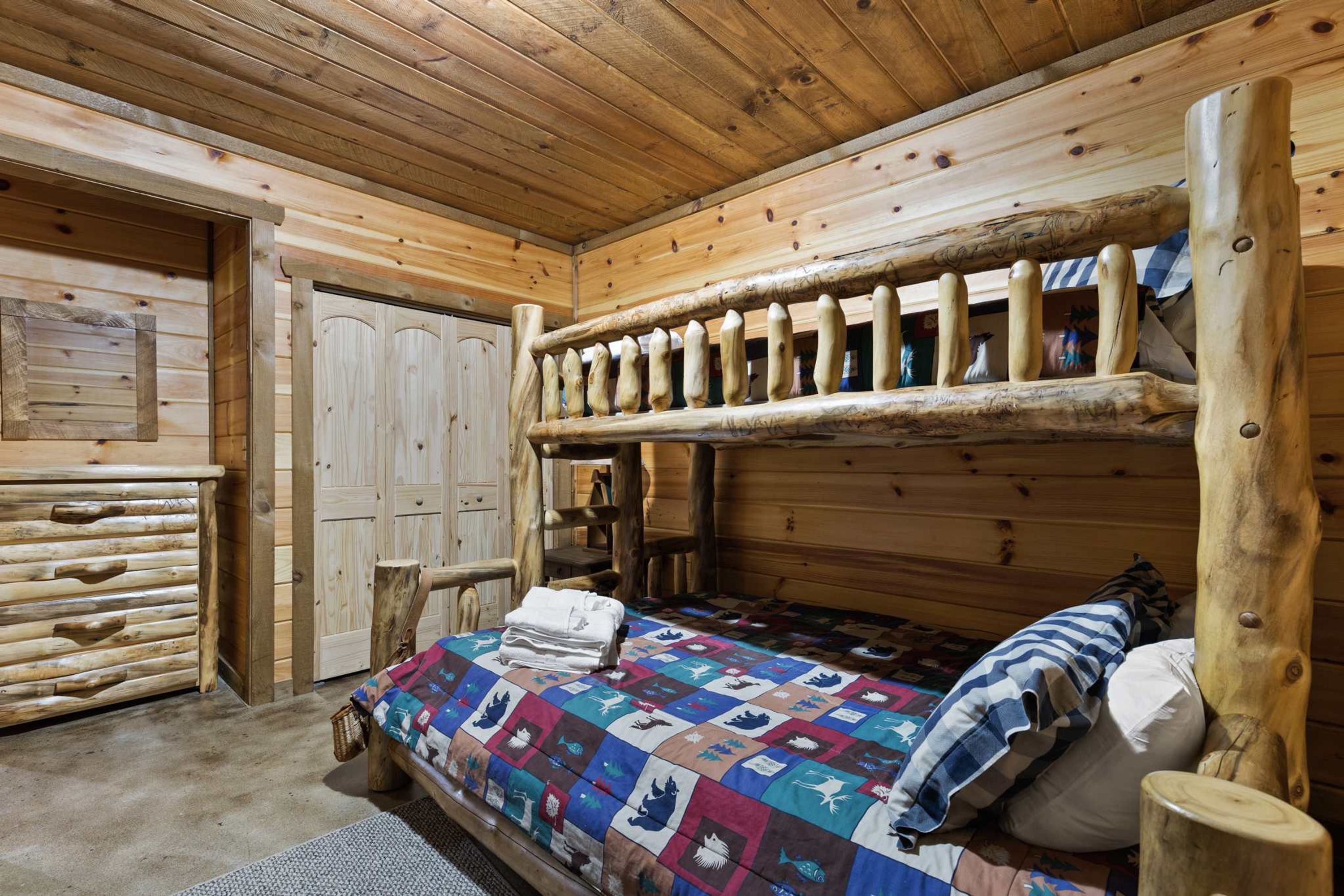 A rustic wooden cabin interior with a bunk bed, a wooden dresser, and a door.