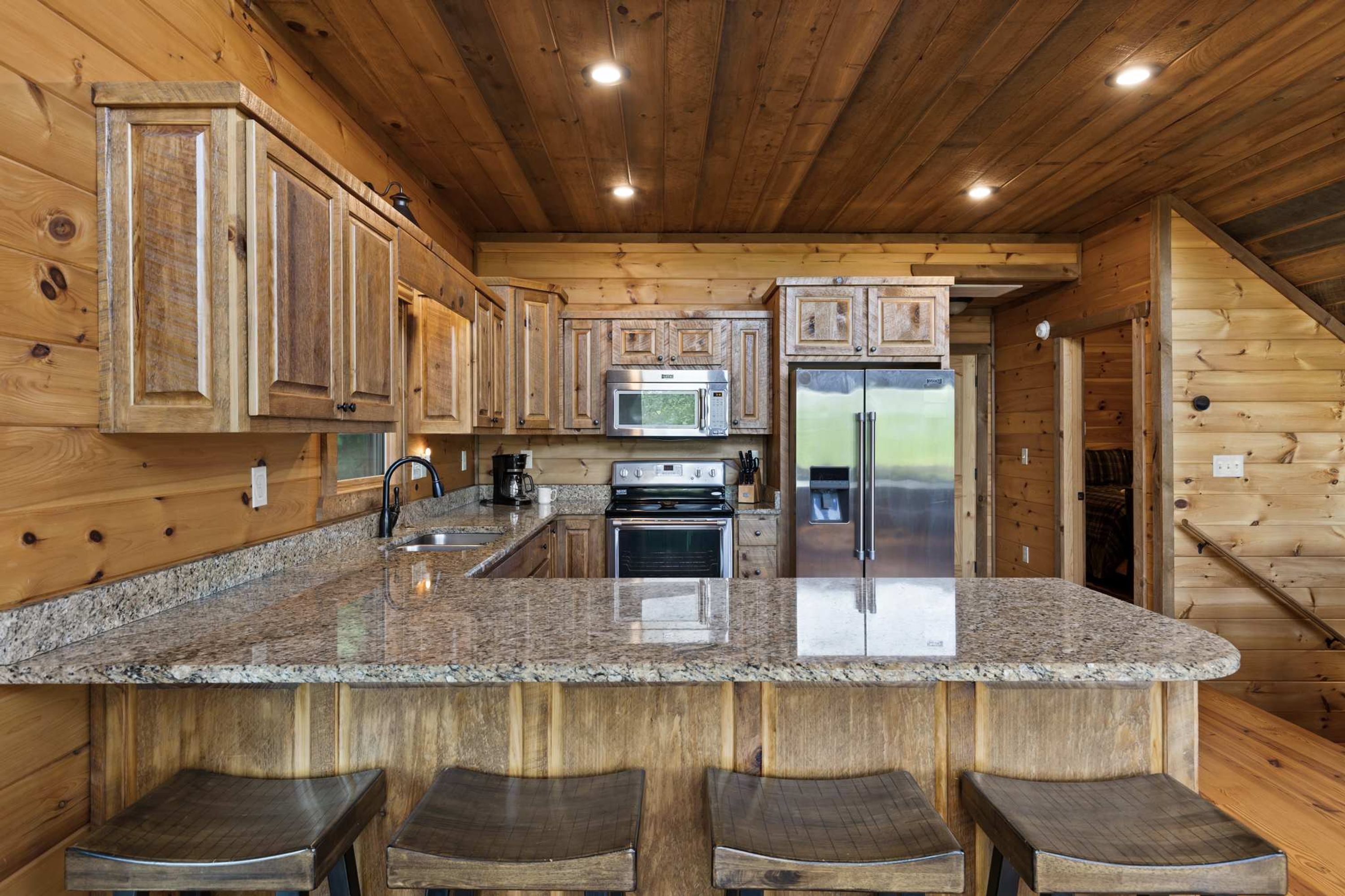 Cocina con armarios de madera, encimera de granito, electrodomésticos de acero inoxidable y una zona de asientos con taburetes.