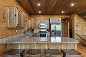 Cocina con armarios de madera, encimera de granito, electrodomésticos de acero inoxidable y una zona de asientos con taburetes.