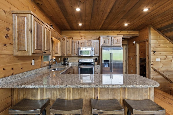 A kitchen with wooden cabinetry, a granite countertop, stainless steel appliances, and a bar stool seating area. - Mtn Cabin w Hot Tub Game Room Grill Views (Blue Ridge)