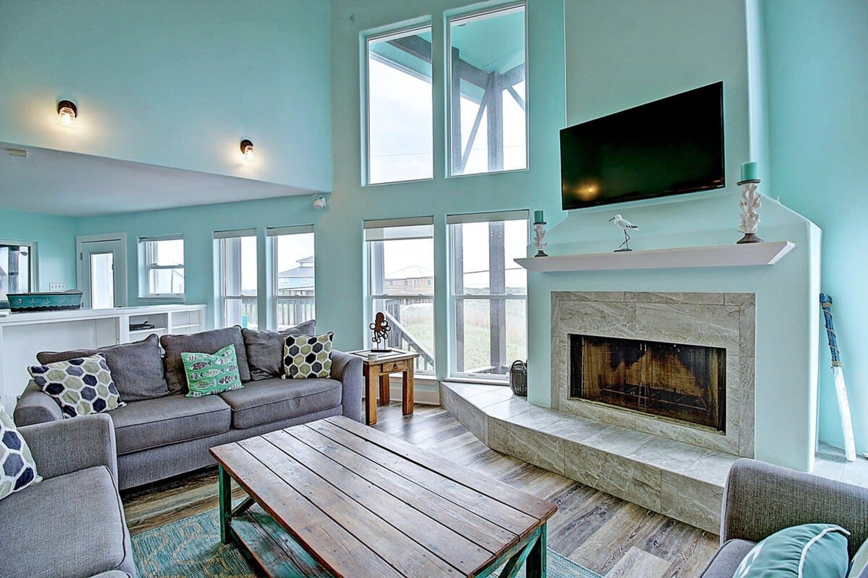 A spacious living room with a fireplace, large windows, and a flat-screen TV mounted above it.
