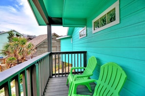 A turquoise house with a wooden deck, two green plastic chairs, and a view of neighboring houses. - La Playa Paradise- Beach Access Large Island Home Pool Table (Port Aransas)