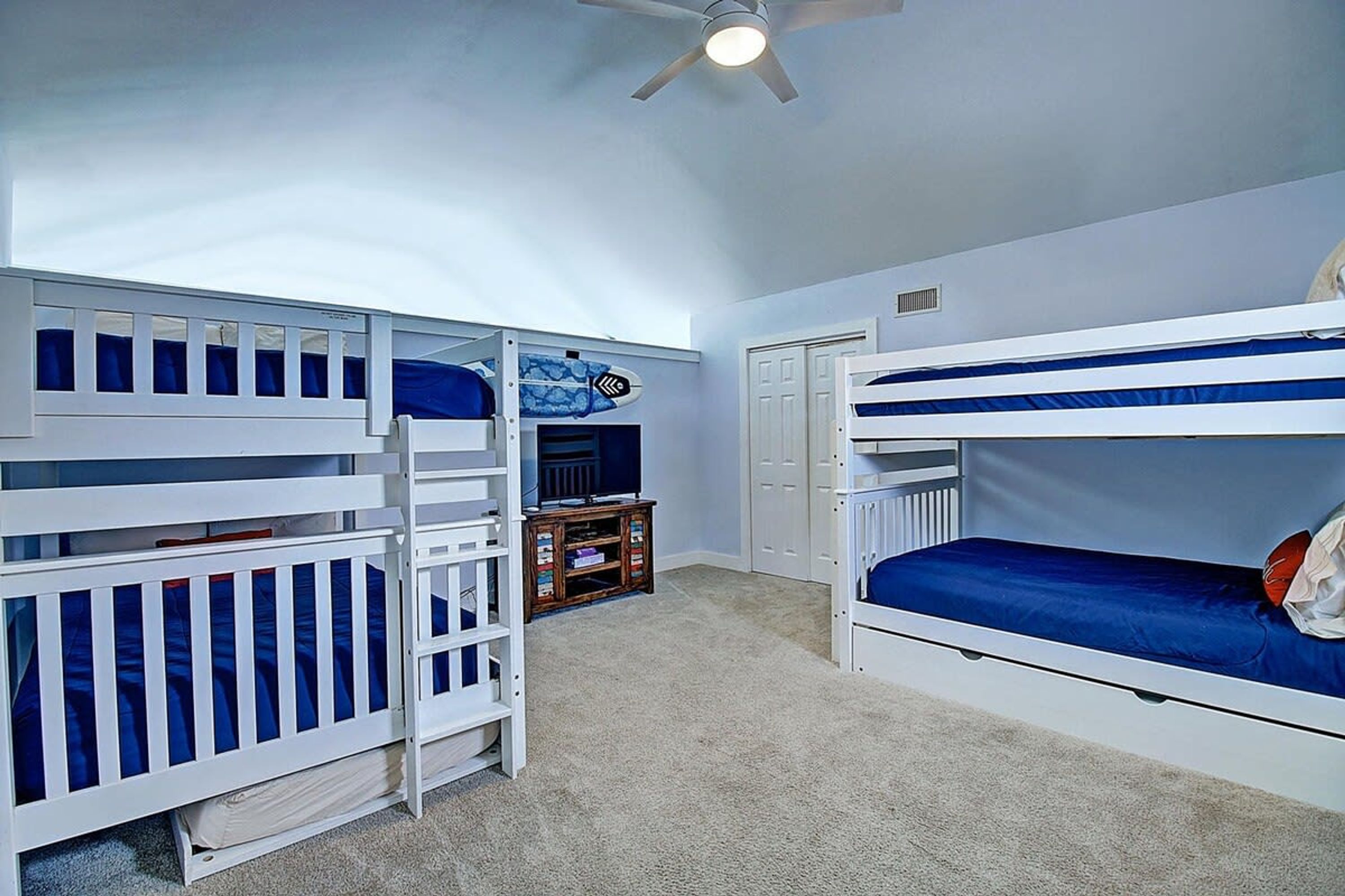 A room with bunk beds, a ceiling fan, and a small wooden cabinet.