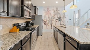 A modern kitchen with dark cabinetry, granite countertops, and a decorative wall mural. - Magic Moments Villa Private Pool Spa Games (Kissimmee)
