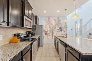 A modern kitchen with dark cabinetry, granite countertops, and a decorative wall mural. - Magic Moments Villa Private Pool Spa Games (Kissimmee)