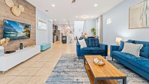 A modern living room with a blue sofa set, a wooden coffee table, and a TV mounted on the wall. - Magic Moments Villa Private Pool Spa Games (Kissimmee)