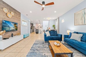 A modern living room with a blue sofa set, a wooden coffee table, and a TV mounted on the wall. - Magic Moments Villa Private Pool Spa Games (Kissimmee)