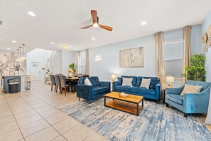 Un salon moderne avec un canapé bleu, une table basse et un coin repas agrémenté d’un lustre.