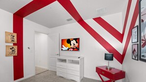 A room with a white and red color scheme, featuring a white cabinet, a red side table, and a wall-mounted TV displaying an animated character. - Magic Moments Villa Private Pool Spa Games (Kissimmee)