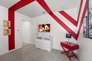 A room with a white and red color scheme, featuring a white cabinet, a red side table, and a wall-mounted TV displaying an animated character. - Magic Moments Villa Private Pool Spa Games (Kissimmee)