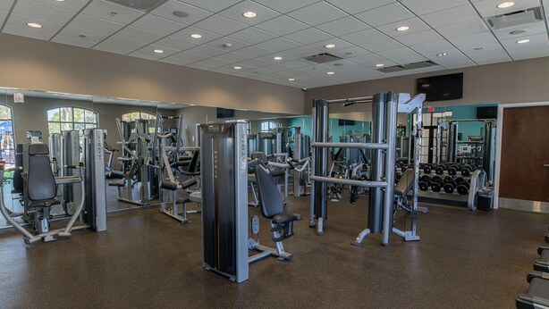 A gym with various exercise machines, weight racks, and a mirrored wall. - Magic Moments Villa Private Pool Spa Games (Kissimmee)