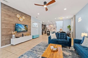 Ein modernes Wohnzimmer mit Flachbildfernseher, Deckenventilator und Essbereich mit Tisch und Stühlen.