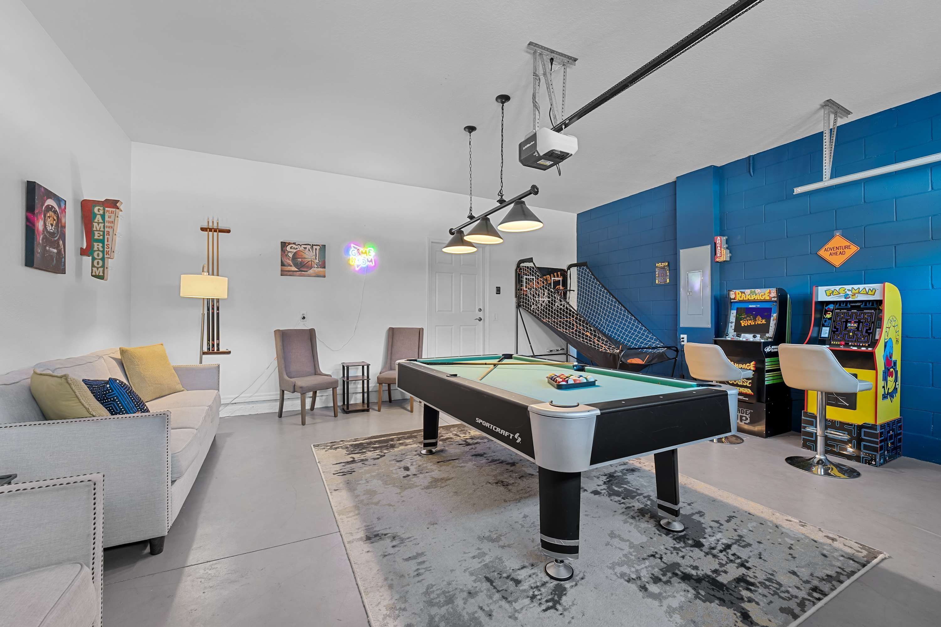 A pool table in a room with a blue wall, arcade games, and a staircase.