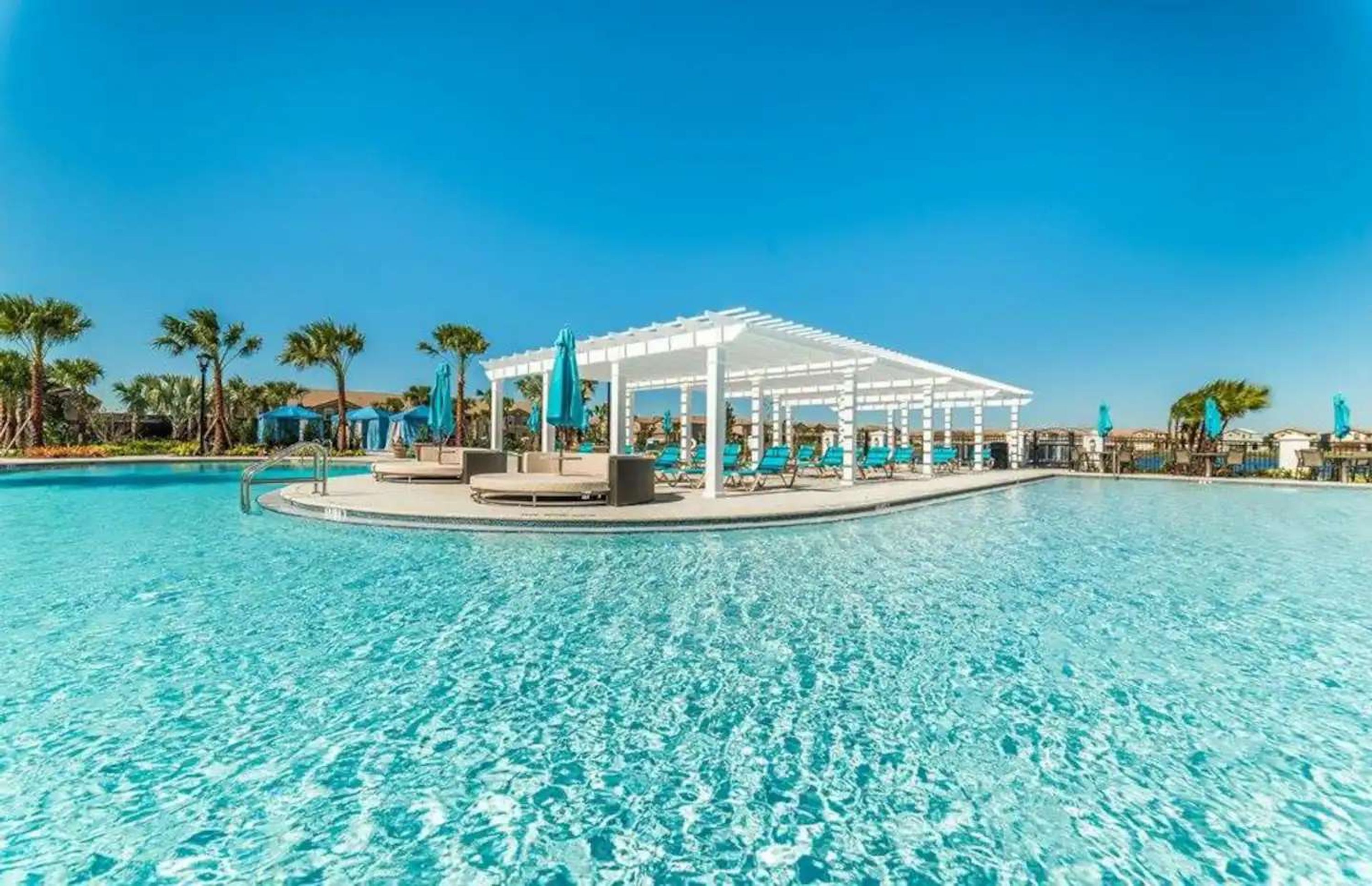 En klarblå pool med en vit pergola och solstolar.