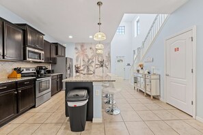 Une cuisine moderne avec des meubles de couleur sombre, des appareils en acier inoxydable et un îlot central doté de tabourets de bar.