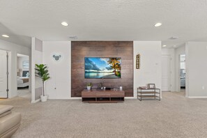 Ein modernes Wohnzimmer mit einem großen Flachbildfernseher an einer Holzwand, einer kleinen Holzunterhaltungseinheit darunter und einer Blumentopf auf der linken Seite.