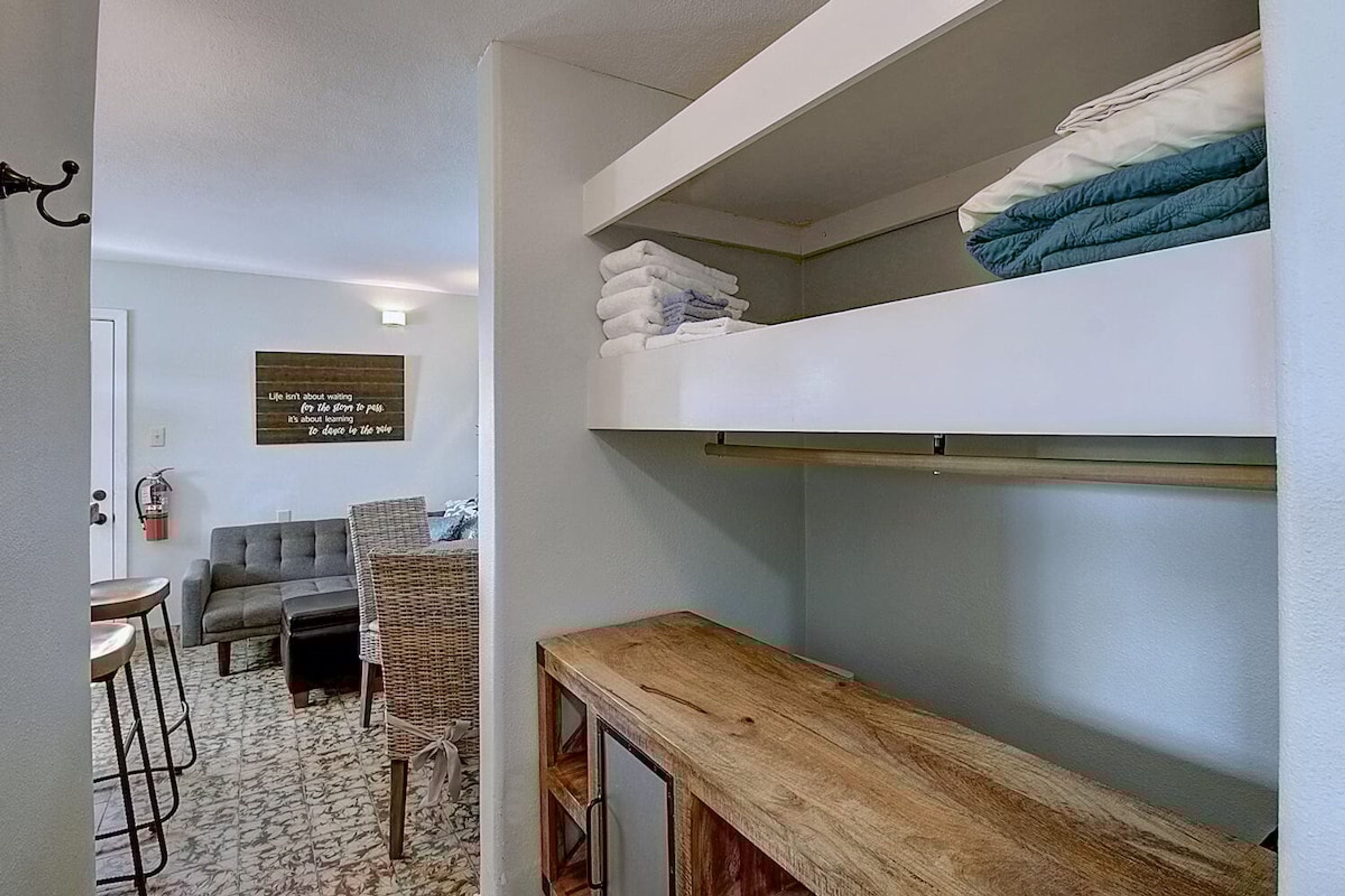 Un espacio habitable compacto con una litera, una pequeña zona de estar y un estante en la pared.