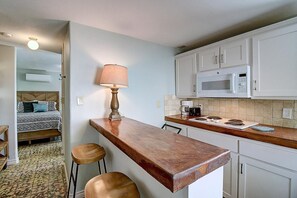 A compact kitchen with a wooden countertop, a microwave, a coffee maker, and a dining area with a bed and a patterned rug. - Kahuna Cottage- Family Friendly Fenced Yard (Port Aransas)