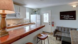Cocina con encimera de madera, armarios blancos, microondas y refrigerador. Hay un taburete de bar y una lámpara fijada a la pared.