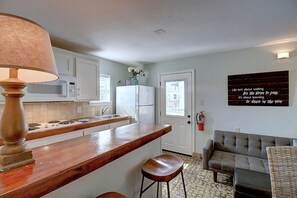 Eine Küche mit Holztischplatte, weißen Schränken, einer Mikrowelle und einem Kühlschrank. Ein Barhocker und eine Wandleuchte sind vorhanden.