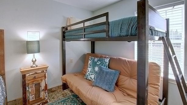 Una cama litera con un sofá y una lámpara, un armario de madera y una ventana con persianas.