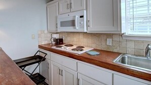 Una cocina con armarios blancos, microondas, estufa y pileta.