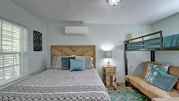 Un dormitorio con una cama individual superpuesta, una cama individual con ropa de cama estampada, una mesita de noche con una lámpara y una ventana con persianas.