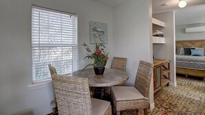 Una habitación con una mesa redonda, sillas de mimbre, una planta en maceta y una cama con ropa de cama estampada.