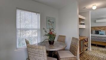Una habitación con una mesa redonda, sillas de mimbre, una planta en maceta y una cama con ropa de cama estampada.