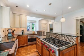 A modern kitchen with wooden cabinets, a built-in stove, and a large island with a tiled backsplash. - 6BR Home Private Pool Spa Games Gazebo (Memphis)