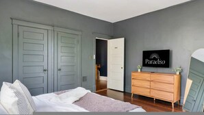 Ein Schlafzimmer mit Bett, Kommode, Deckenventilator und Fernseher an der Wand.